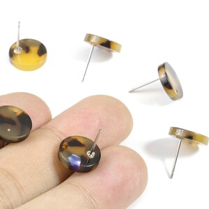 May include: Round stud earrings with a tortoiseshell pattern in shades of brown and yellow. The earrings have a post backing and are displayed against a white background.