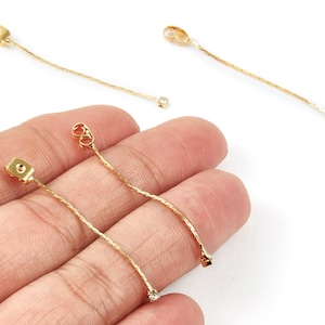 May include: Gold-coloured earring findings with a textured chain design. Each earring has a small, clear gemstone at the end of the chain. The findings are shown against a white background.