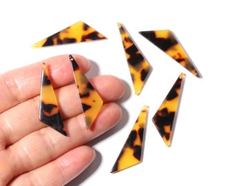Puede incluir: Una colección de colgantes geométricos con estampado de carey. Los colgantes tienen varias formas, incluyendo triángulos y trapecios, con un agujero para ensartar. La combinación de colores es una mezcla de ámbar, negro y marrón.