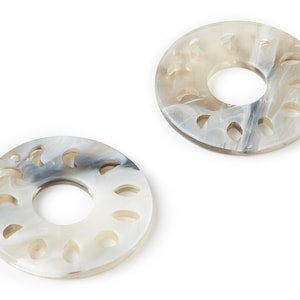 May include: Two white and gray round coasters with a decorative cutout design. The coasters have a hole in the center.