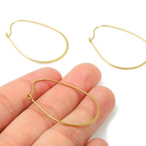 May include: Gold-coloured oval-shaped earring findings. The earrings are made of thin wire and have a simple, minimalist design. The findings are shown against a white background.
