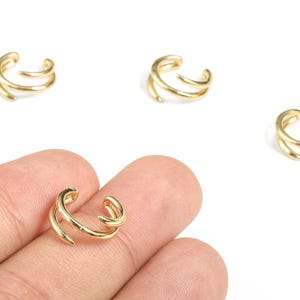 Può includere: Polisini per orecchie color oro con un design a doppia fascia. I polsini per orecchie sono mostrati su sfondo bianco. L'immagine mostra quattro polsini per orecchie, uno dei quali è tenuto dalle dita di una persona.