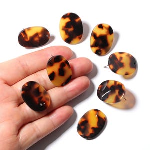 May include: Oval-shaped tortoise shell beads with a glossy finish. The beads are a mix of amber and dark brown, with a hole drilled through each for stringing. These beads are suitable for jewelry making.