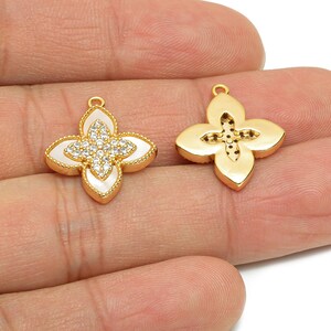 May include: Two gold-colored flower-shaped pendants. One pendant features a white center with a sparkling crystal design, while the other has a solid gold finish. Both have a small loop for attaching to a chain or other jewelry component.