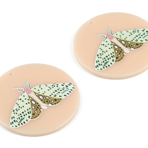 May include: Two round, peach-coloured ornaments with a green and brown moth design. Each ornament has a small hole at the top for hanging.