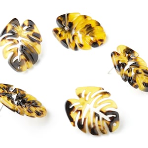 May include: Four pairs of brown and yellow patterned earrings shaped like monstera leaves.