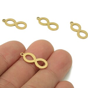 May include: Gold-coloured infinity symbol charms. The charms are small, with a loop at the top for attaching to jewellery. The infinity symbol is a figure eight shape. The charms are shown against a white background.