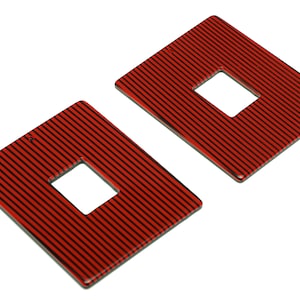 May include: A pair of red and black striped earrings with a square shape and a rectangular hole in the center.