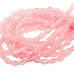 Może przedstawiać: Kolekcja jasnoróżowych, fasetowanych koralików w kształcie łezki. Koraliki są nawleczone, tworząc płynny, organiczny kształt. Koraliki mają miękki, półprzezroczysty różowy kolor, idealny do tworzenia biżuterii.