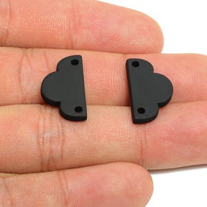 May include: Two matte black cloud-shaped components, each with two small holes and a flat edge. These components are likely for jewelry making or crafting. The components are displayed against a neutral background.