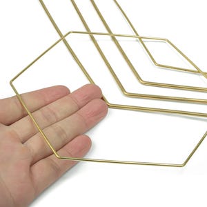 Puede incluir: Una mano sostiene una estructura de alambre geométrica de color dorado. La estructura de alambre tiene forma de hexágono, con varias formas similares en el fondo. El alambre es delgado y parece ser de metal.