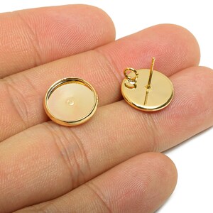 May include: Two gold-colored, round earring components. One is a flat disc with a post and loop, the other is a shallow dish. The components are held in a hand against a white background. These are jewelry making supplies.