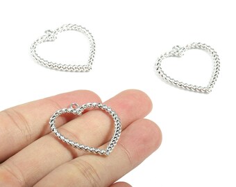 May include: Silver-toned heart-shaped jewelry findings with a textured, beaded design. The heart charms are shown in a close-up view, with one held in a hand. The findings have a small loop at the top for attaching to other jewelry components.