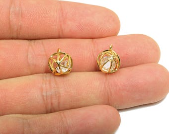 May include: Two small, gold-colored pendant charms. Each charm features a geometric cage design encasing a clear, faceted stone. The charms are displayed on a light-toned background.