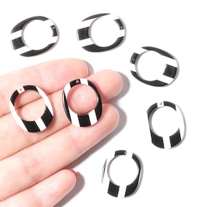 Peut inclure: Composants de bijoux ovales à rayures noires et blanches. Les composants ont un trou en haut pour l'enfilage. Le design est un motif graphique audacieux. Probablement pour boucles d'oreilles ou pendentifs.