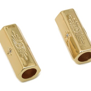 May include: Two gold-toned metal hexagon-shaped beads with a sunburst design and a small clear rhinestone. The beads have a hole in the center for threading.