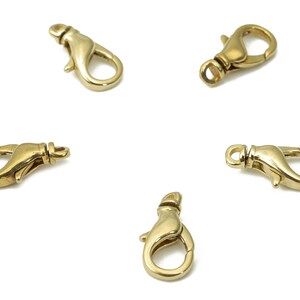 Puede incluir: Cinco cierres de langosta dorados, cada uno con una puerta con resorte y una base giratoria redondeada. Los cierres están dispuestos sobre un fondo blanco, mostrando su diseño y acabado.