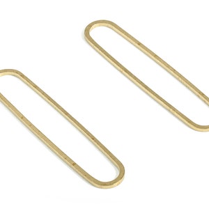 Peut inclure: Deux cerceaux en métal de couleur dorée, chacun en forme d'ovale avec un bord arrondi. Les cerceaux sont posés à plat sur une surface blanche.