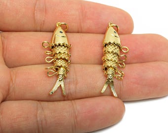 May include: Two gold-colored fish charms. Each charm has a fish shape with a textured body, a loop at the top, and a tail. The charms are displayed against a light background.