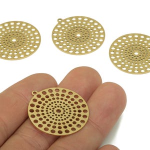 May include: Four brass-coloured, circular pendants with a spiral pattern of small holes. One pendant is held in a hand, while the other three are arranged on a white background. Each pendant has a small loop at the top for attaching to a chain or other jewellery component.