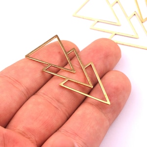 Peut inclure: Charm en métal doré en forme de flèche. Les breloques ont un design géométrique triangulaire avec un centre creux. Plusieurs breloques sont visibles sur fond blanc, suggérant qu'il s'agit de fournitures artisanales.