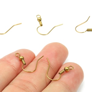 May include: Close-up of several gold-coloured earring hooks. The hooks have a curved design with a small ball and a coil at the top, and a curved wire for the ear. The hooks are shown against a white background.