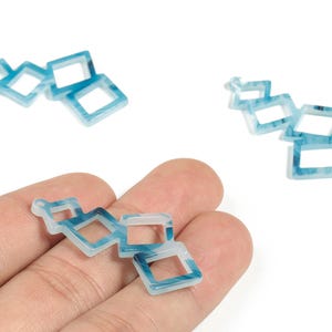 May include: Blue and white square charms with a marbled effect. The charms are linked together in a chain, with a small loop at the end of one chain. These charms are suitable for jewellery making.