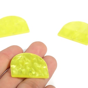 Könnte beinhalten: Drei durchscheinende, halbkreisförmige, gelb-grüne Cabochons aus Harz. Einer wird in einer Hand gehalten, während sich die anderen beiden auf weißem Hintergrund befinden. Die Cabochons haben ein marmoriertes Aussehen.