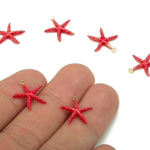Peut inclure: Six petits breloques en forme d'étoiles de mer rouges avec des boucles dorées pour la fabrication de bijoux. Les étoiles de mer sont d'un rouge vif et ont une surface texturée.