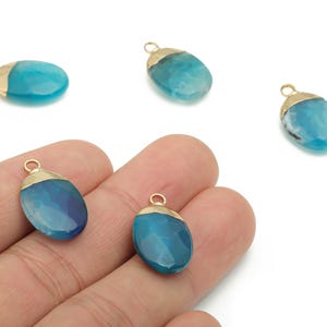 May include: Close-up of several blue and gold gemstone pendants. Each pendant has a gold-colored cap and a blue, oval-shaped stone. The pendants are displayed against a white background.