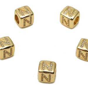 May include: Five gold-tone letter beads, each featuring the letter "N" in raised lettering with clear rhinestones. The beads are square-shaped and have a hole for threading.