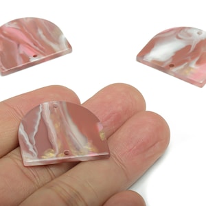 May include: Three pink and white marbled resin pendants in a half-circle shape. Each pendant has two holes for stringing. One pendant is held in a hand.