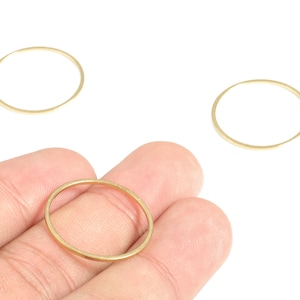 May include: Three gold-coloured, thin metal rings. One ring is held in a hand, while two others are separate. The rings are circular and have a smooth, polished finish. The background is plain white.