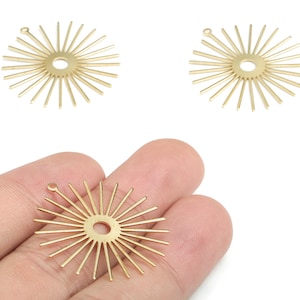 Puede incluir: Tres colgantes dorados con forma de sol con un agujero central y líneas radiales. Un colgante se sostiene en una mano. Estos colgantes son adecuados para la fabricación de joyas y otros proyectos de artesanía.