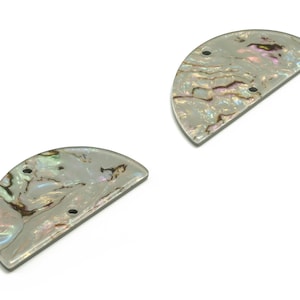 Może przedstawiać: Dwa półokrągłe, opalizujące kawałki muszli z perłowej masy perłowej z wywierconymi otworami.