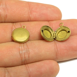 May include: Two small, round, antique brass lockets. One is closed, and the other is open, revealing an oval interior. Both have a small loop at the top for attaching to a chain or cord. These are ideal for jewelry making.