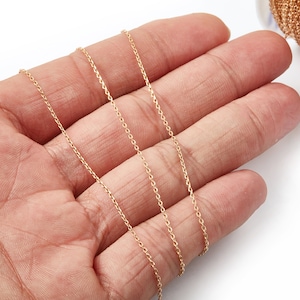 May include: A close-up of a gold chain, shown in a hand, with a spool of the same chain in the background.