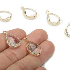 May include: Clear teardrop-shaped crystal pendants with gold-colored metal edging. The pendants have a small loop at the top for attaching to a chain or other jewelry component. The crystals are faceted, catching the light.