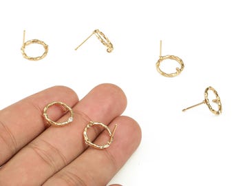 May include: Gold-colored stud earrings with a textured, organic design. The earrings are circular, with a small post for insertion into the ear. One earring features a small, clear gemstone. The earrings are displayed on a white background.