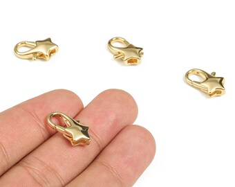 May include: Gold-colored star-shaped lobster clasps. Four clasps are scattered on a white background, with one held in a person's hand. The clasps are made of shiny metal and have a simple, elegant design, perfect for jewelry making.