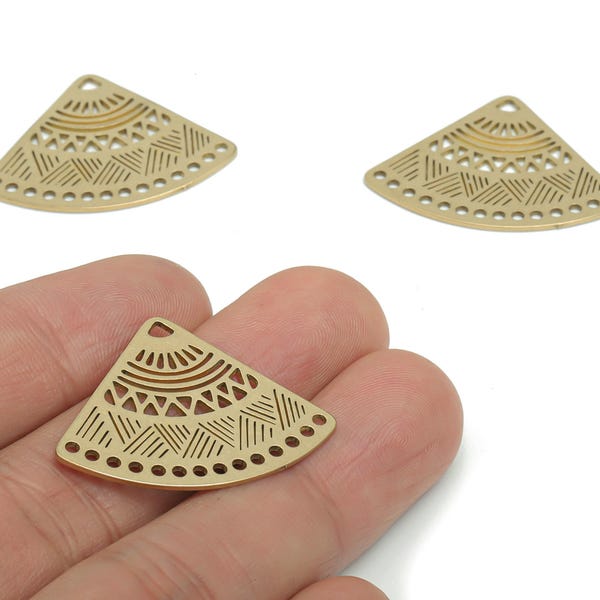 Puede incluir: Tres dijes de metal dorados en forma de abanico con intrincados cortes geométricos. Un dije se sostiene en una mano, mostrando el diseño detallado. Cada dije tiene un pequeño agujero en la parte superior para ensartar.