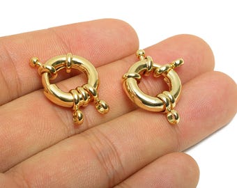 May include: Two gold-colored, round spring ring clasps. Each clasp has a circular design with a spring mechanism and decorative accents. The clasps are shown against a neutral background, highlighting their metallic sheen.