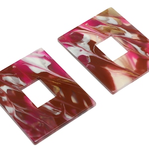 Puede incluir: Dos pendientes de forma cuadrada con un diseño de mármol en tonos rosa, marrón y blanco. Cada pendiente tiene un recorte cuadrado en el centro.