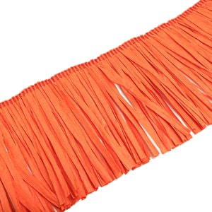 Peut inclure: Frange en papier orange. La frange est composée de fines bandes de papier attachées à une base tissée.