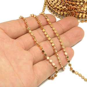 May include: Gold chain with small round links. The chain is laid out in a straight line on a hand.