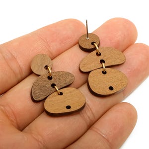 May include: Wooden dangle earrings with a geometric design. The earrings feature various shapes in shades of brown, connected by gold-colored hoops. The earrings have a post for pierced ears.