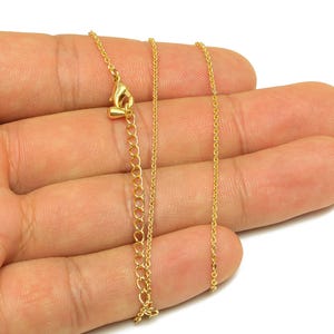 Op de afbeelding: Een delicate goudkleurige ketting met een ketting en een verstelbare verlenging. De ketting wordt in een hand gehouden tegen een witte achtergrond. De ketting is dun en heeft kleine schakels.