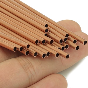 May include: A collection of small, copper-coloured metal tubes, each with a hollow centre. The tubes are held in a hand, and are arranged in a bundle. The tubes are approximately 0.3 cm in diameter.