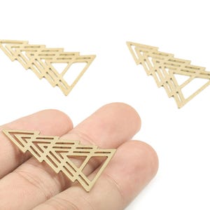 May include: Three gold-coloured geometric triangle charms. Each charm is composed of multiple connected triangles, creating a layered effect. One charm is held in a hand, while two others are separate. These charms are suitable for jewellery making.