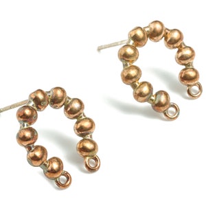 May include: A pair of gold-toned earrings with a horseshoe shape made of small beads. The earrings have a silver post and a small loop at the bottom.